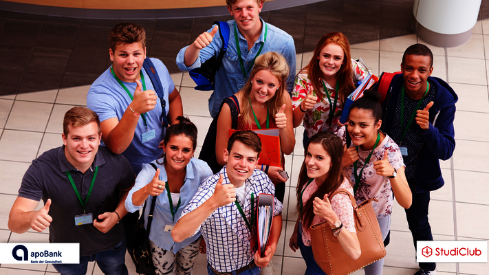 Gruppe junger Menschen, die fröhlich nach oben schauen und den Daumen hoch zeigen.
